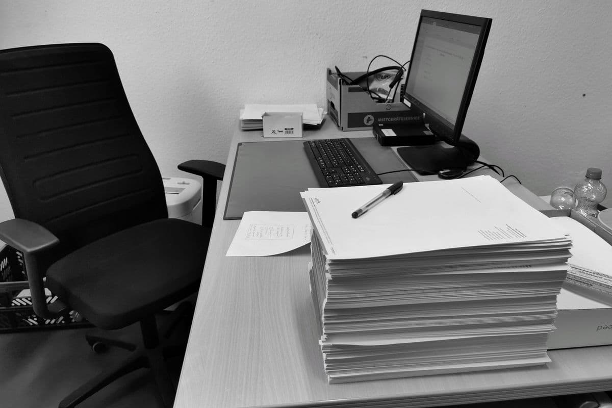 Corporate desk with stacked paper documents beside a computer